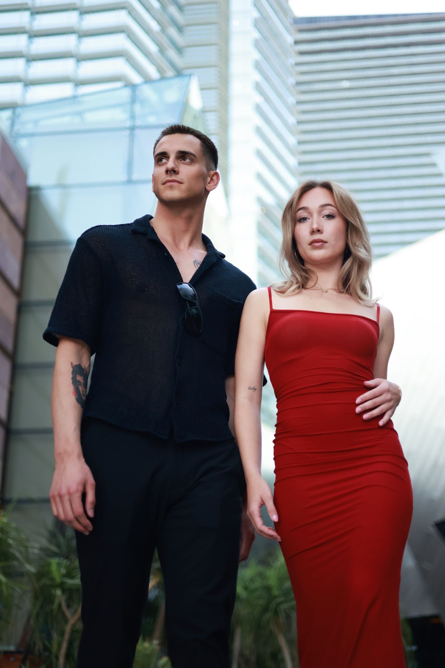 Couple in a black outfit and a red dress between glass towers