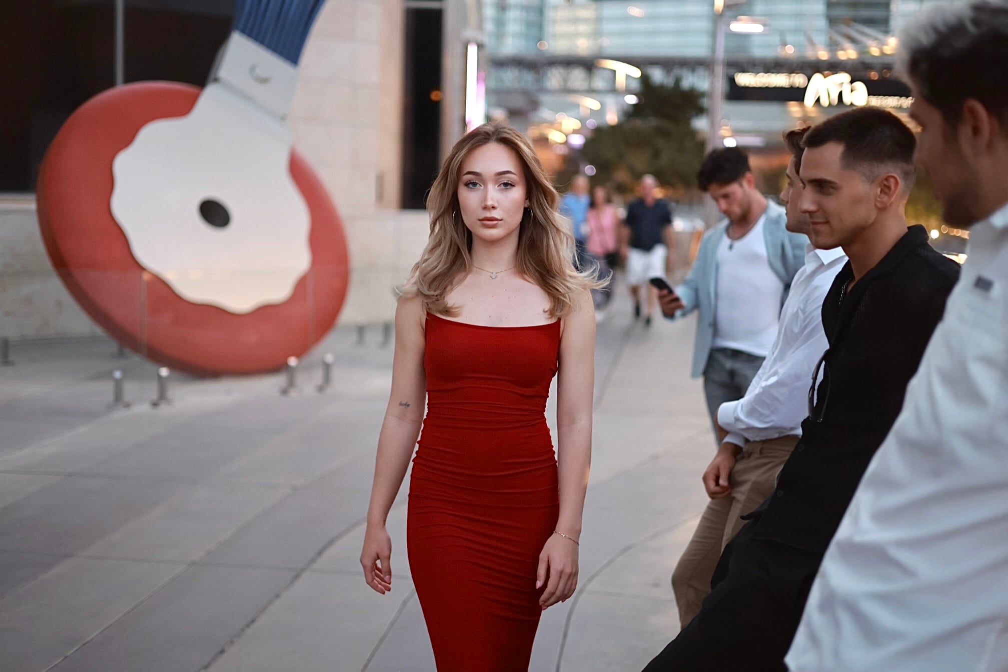 Woman in a red dress crossing a plaza past a sculpture