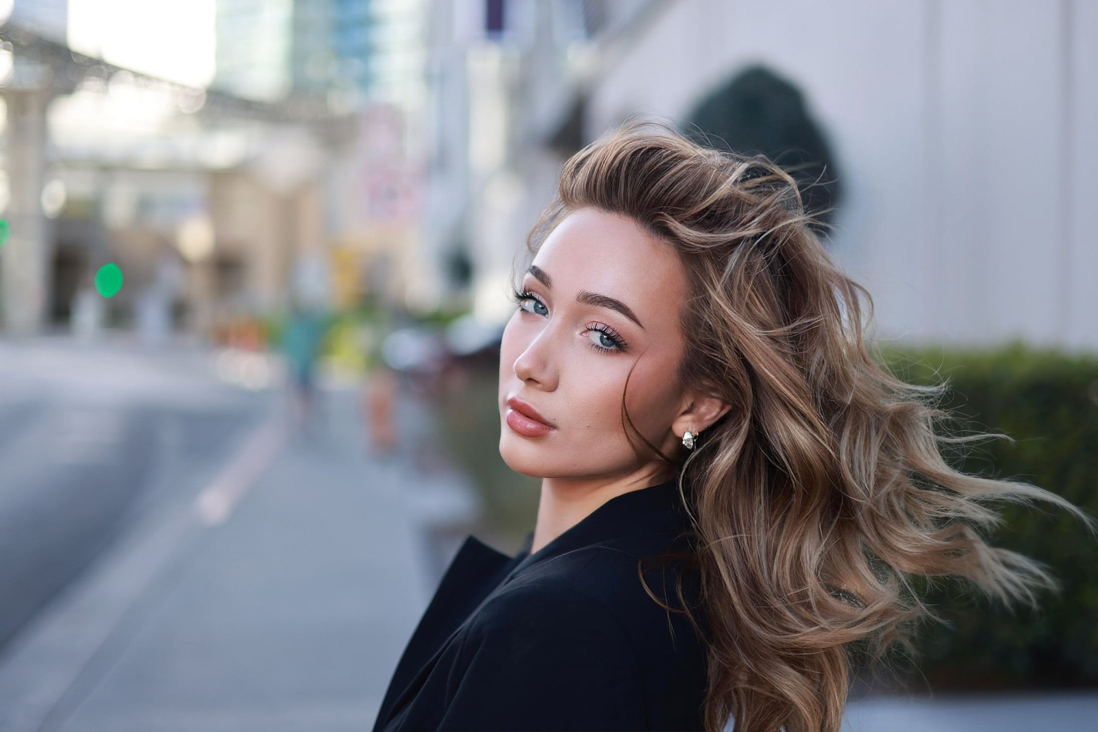 Woman in a black blazer on a city street, hair in the wind